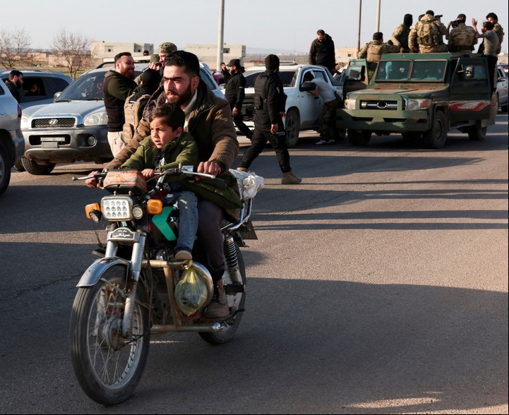 Un civil con us hijo pasa junto a un convoy militar en Latakia. Foto: Reuters